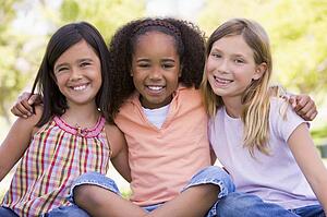 Three young girl friends sitting outdoors smiling