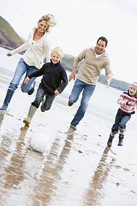 Family playing soccer at beach smiling