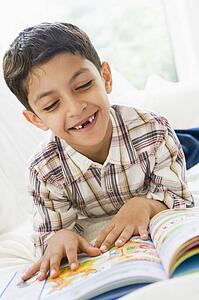 Young boy in living room reading a book and smiling (high key)