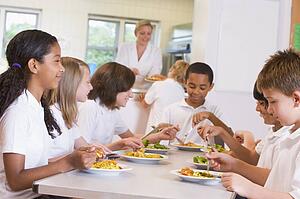 Students sitting at cafeteria table eating lunch (depth of field)