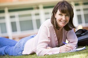 Adult student lying on lawn of school with notebook