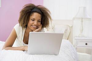 Teenage Girl Lying On Bed Using Laptop 