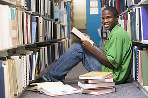 Man sitting on floor in library holding book