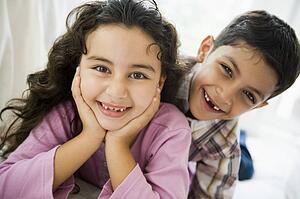 Two young children playing in living room smiling (high key)