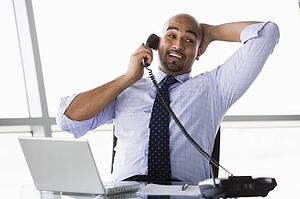 Businessman in office on telephone by laptop smiling (high key/selective focus)