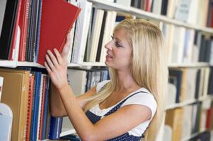 Woman in library pulling book off a shelf (depth of field)