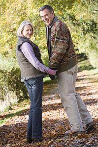 Couple outdoors on path in park holding hands and smiling (selective focus)