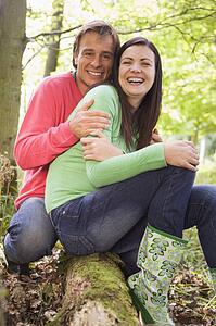 Couple outdoors in woods sitting on log smiling