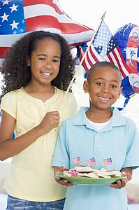 Brother and sister on fourth of July with flag and cookies smiling