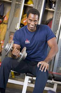 Fireman lifting dumbbell on bench in fire station locker room