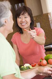 Woman Offering Husband A Piece Of Freshly Chopped Pepper