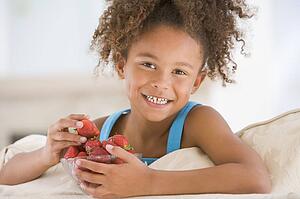 Young girl eating strawberries in living room smiling