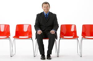 Businessman Sitting In Row Of Empty Chairs 