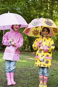Two sisters outdoors in rain with umbrellas smiling