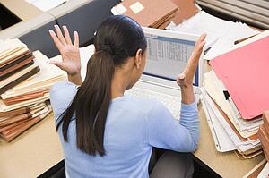 Businesswoman in cubicle with laptop and stacks of files