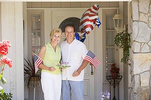 Couple at front door on fourth of July with flags and cookies smiling