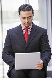 Businessman sitting outdoors by building with a laptop (high key/selective focus)