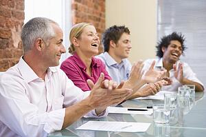 Four businesspeople in boardroom applauding and smiling