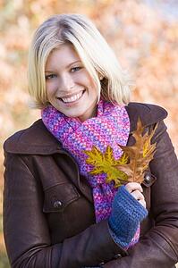Woman outdoors at park holding leaves in hand smiling (selective focus)