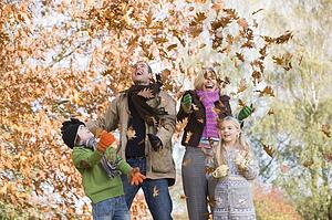 Family outdoors in park playing in leaves and smiling (selective focus)