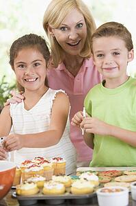 Woman with two children in kitchen decorating cookies smiling