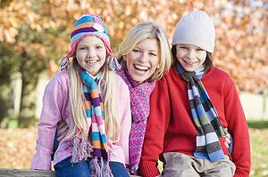 Mother and two young children outdoors in park smiling