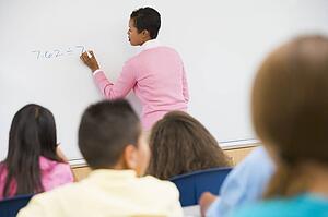 Students in math class with teacher writing on front board (selective focus)