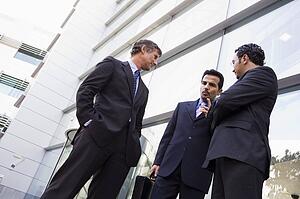 Three businessmen standing outdoors by building talking (high key/selective focus)