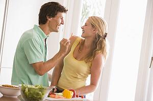 Couple in kitchen cutting up vegetables and smiling