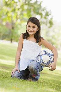 Young girl outdoors at park holding ball and smiling (selective focus)