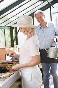 Woman in greenhouse planting seeds and man holding watering can smiling