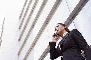 Businesswoman standing outdoors by building on cellular phone (high key/selective focus)
