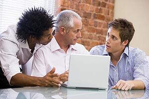 Three businessmen in office with laptop talking
