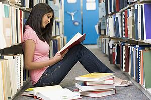 Woman sitting on floor in library reading book