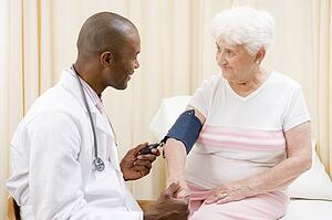 Doctor checking woman's blood pressure in exam room smiling