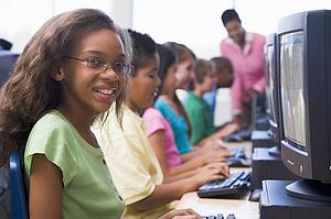 Six children at computer terminals with teacher in background (depth of field/high key)