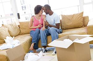 Couple relaxing with champagne by boxes in new home smiling