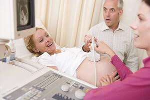 Pregnant woman getting ultrasound from doctor with husband watching