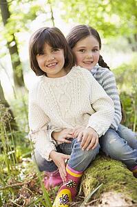 Two sisters outdoors in woods sitting on log smiling
