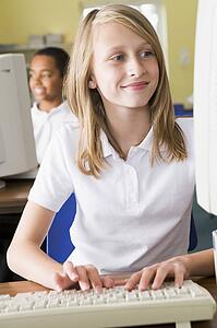 Student at computer terminal typing with student in background (selective focus)