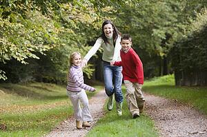 Mother and two young children running on path outdoors (selective focus)