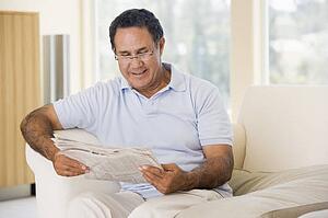 Man in living room reading newspaper smiling