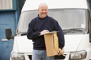 Deliveryperson standing with van with clipboard and box smiling