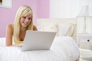 Teenage Girl Lying On Bed Using Laptop 