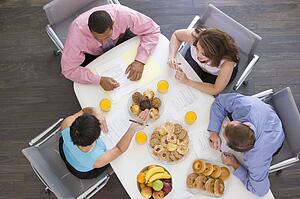 Four businesspeople at boardroom table with breakfast