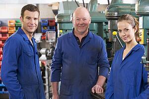 Three machinists in workspace by machine talking