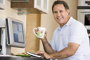 Man in kitchen with computer and coffee smiling