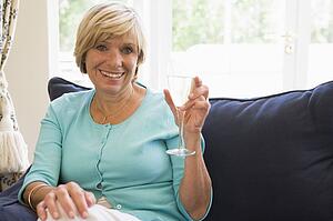 Woman sitting in living room with drink smiling