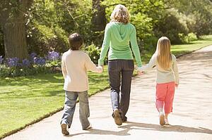 Mother and two young children walking on path holding hands smiling
