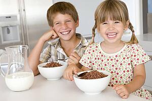 Two young children in kitchen eating cereal smiling